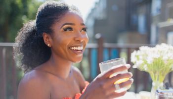 Happy young woman drinking orange juice on sunny balcony