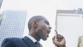 Businessman using breath freshener outdoors, low angle view