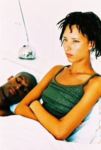side profile of a woman sitting awake with a man sleeping beside her