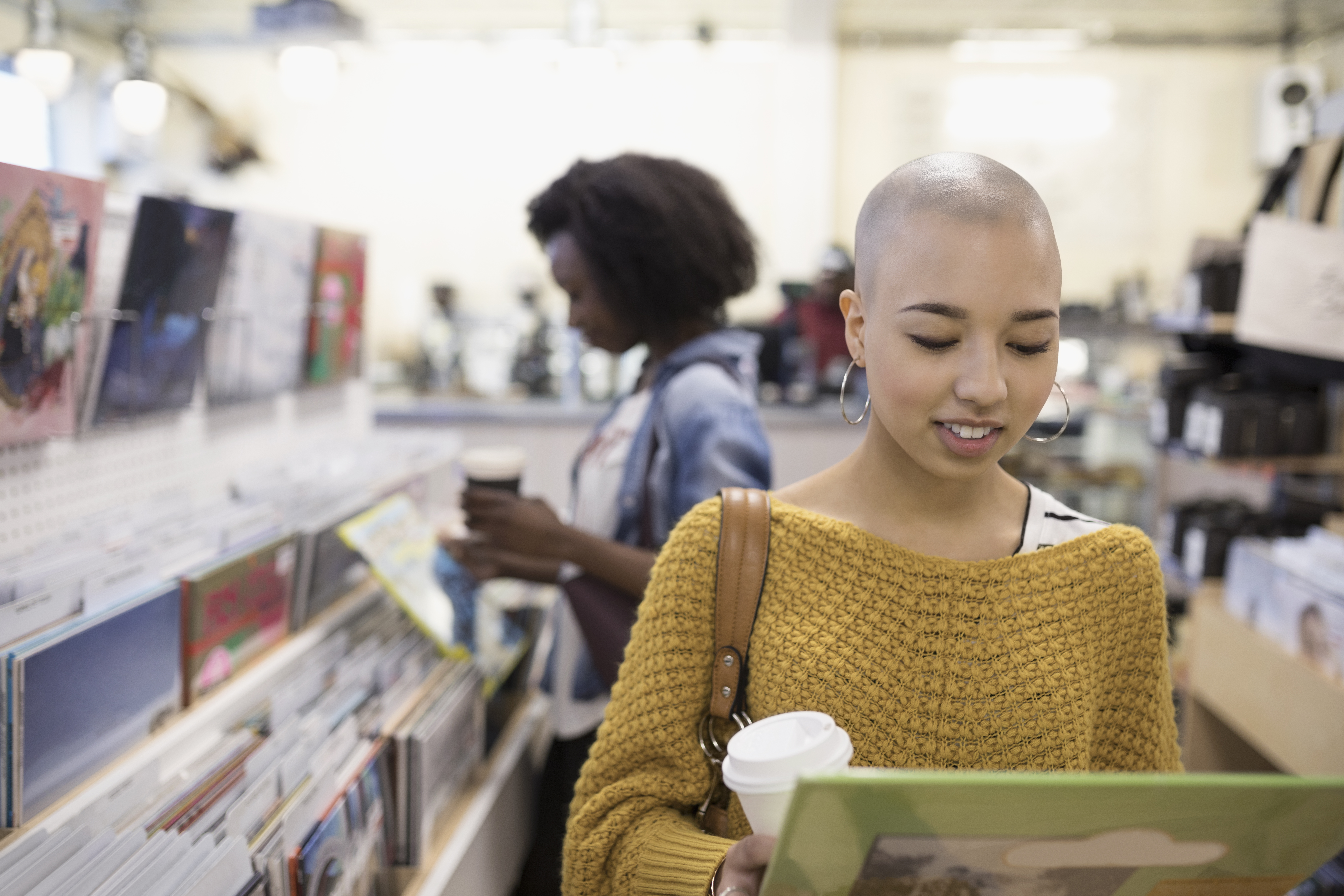 Teenage girl with shaved head drinking coffee and shopping for vinyl records in store