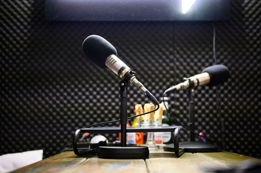 Two black microphones on stands in a recording studio with sound-dampening panels on the walls.